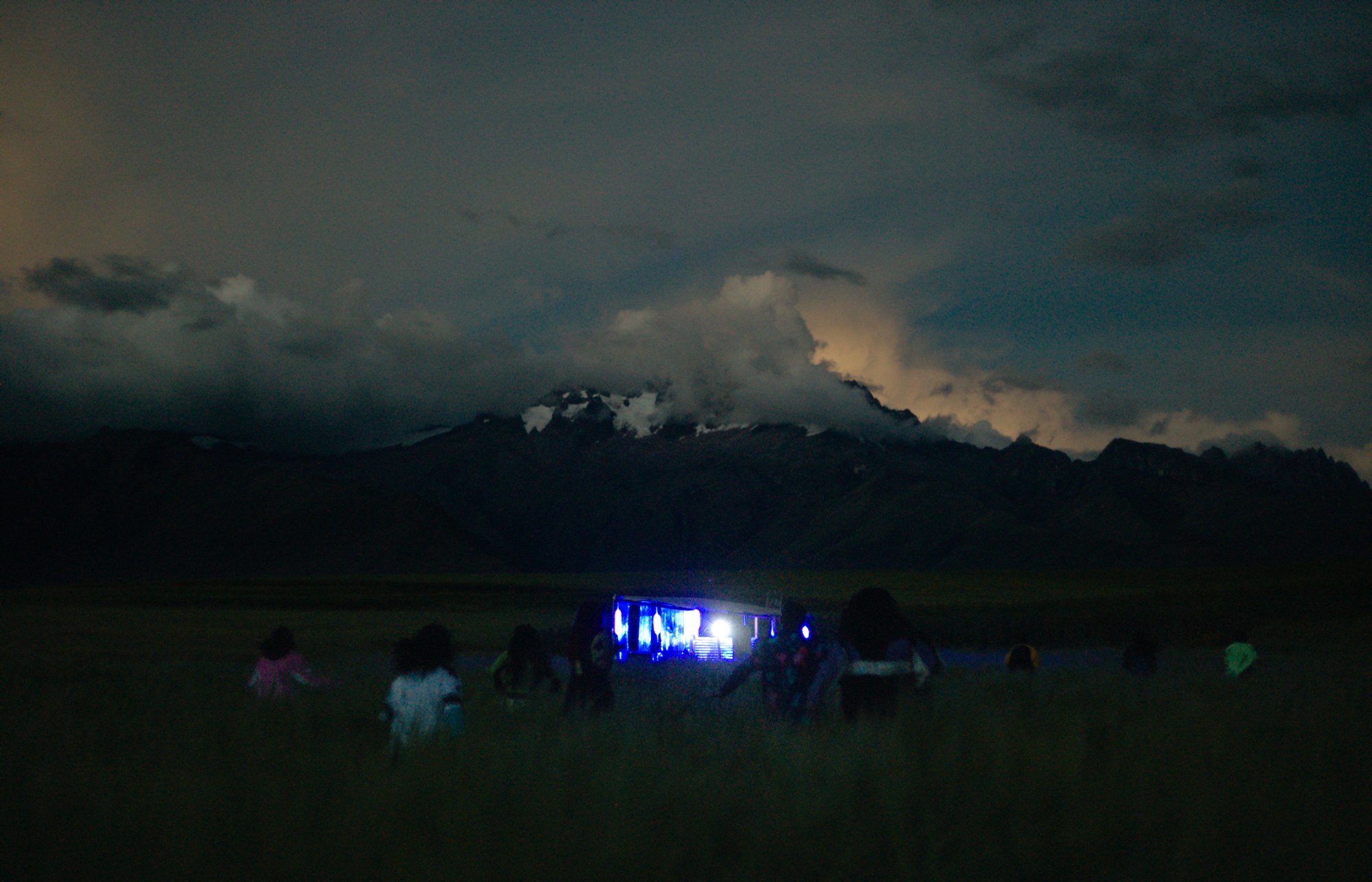 Still de 4EBER: chicos corriendo de noche por un campo hacia un escenario iluminado, con los Andes al fondo